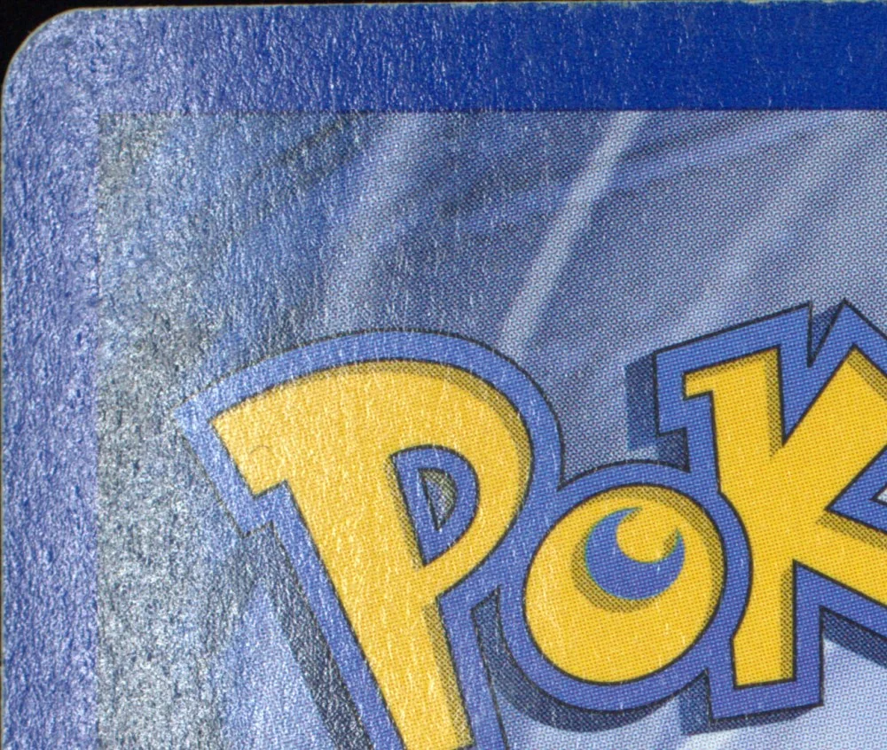 Close-up of the top-left corner of the Crystal Lugia back: the printed blue border is rough, pitted and mottled